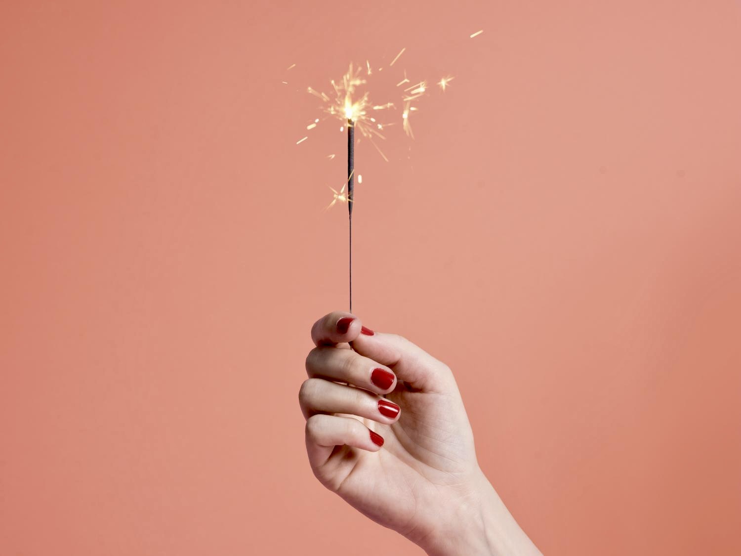 Une main aux ongles laqués tient un cierge magique allumé